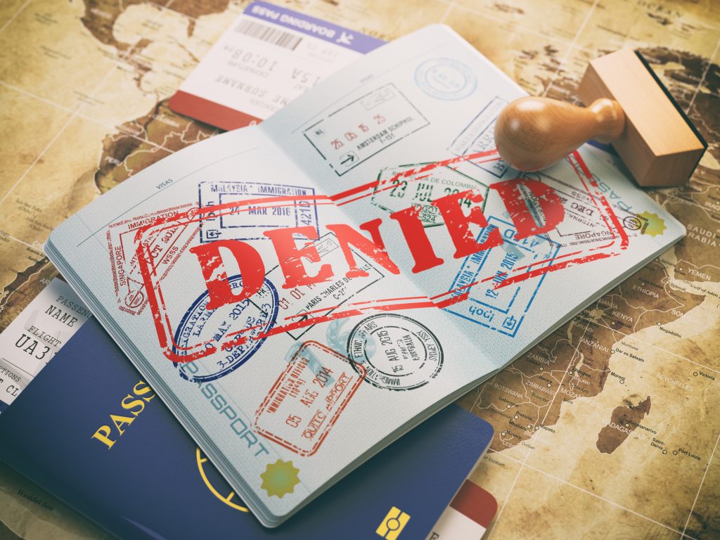 pictured of a passport that has been stamped with the word DENIED on it in big red letters