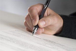 man's hand holding a pen writing his signature
