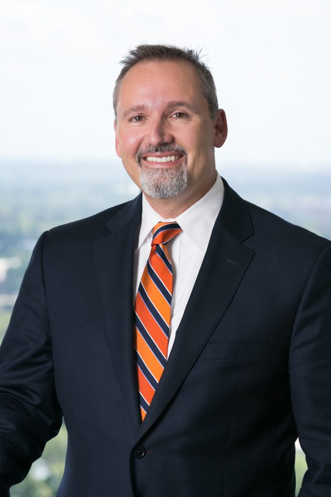 Picture of Mike Mercurio wearing a black jacket, white shirt, and a blue, light orange, and dark orange tie