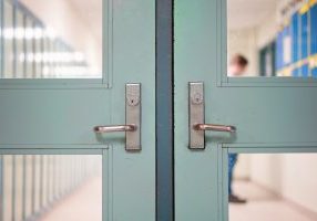 Student returning to school. School reopening following social distancing rule after covid-19 pandemic lockdown. Door and handle see through lockers and student standing at background in school.