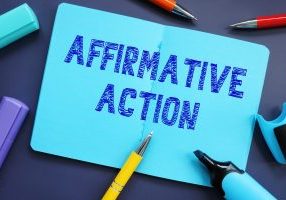 Affirmative action written in ink on blue notepad paper surrounded by pens and hi-lighters
