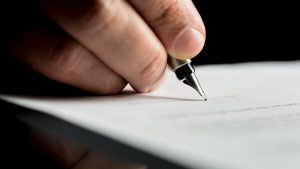 Macro shot of a hand of a businessman signing or writing a document on a sheet of white paper using a nibbed fountain pen.