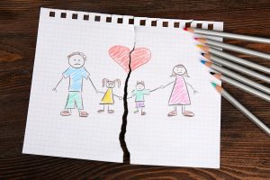 Torn apart drawing of a family on wooden background with colored pencils on the side