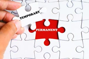 PERMANENT (word) on missing puzzle piece with a hand hold a piece that says TEMPORARY